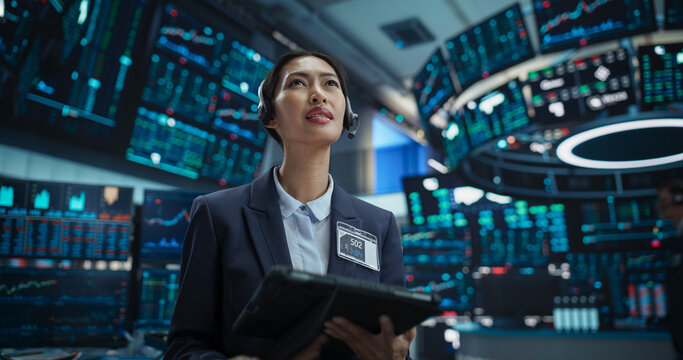 Professional Stock Exchange Trader Working in a Trading Company. Asian Female Stockbroker Talking with Business Clients on a Call, Working on Tablet, Predicting Financial Data for Customer