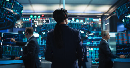 Obraz premium Female Investment Banker Wearing Headphones and Using a Tablet Computer with Financial Market Analytics Data. Team Leader Monitoring Daily Operations, Working of Behalf of Corporate Business Partners