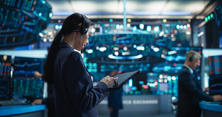 Successful Stock Exchange Manager Wearing Headphones, Working in Modern Office. Proactive Female Trader Browsing Financial Reports on a Tablet Computer, Using Software with Stock Market Auctions