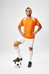 Obraz premium handsome african american man in sportwear with football with arms akimbo and looking at camera