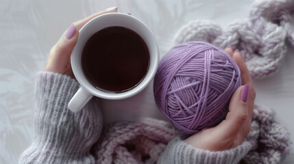 Female hands holding a cup of black coffee and a ball of purple yarn on a white table