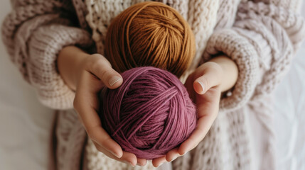 Fototapeta na wymiar Female hands in a beige sweater hold a ruby ball of yarn and an ocher ball of yarn