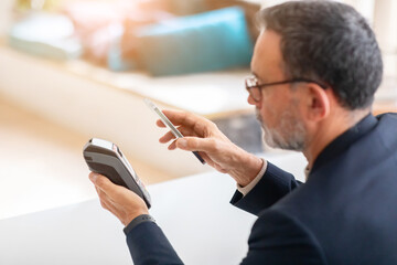 A mature businessman in a smart suit uses contactless payment with his smartphone