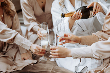 Photo with bridesmaids drinking champagne from glasses in the morning in a beautiful hotel. Photo of a beautiful young bride and her friends in matching dresses drinking champagne before the wedding.
