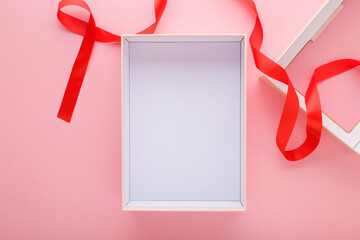 Opened empty white gift box with red ribbon on light pink table background. Pastel color. Closeup....