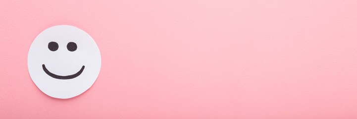 Drawn black smiley on white paper. Happy smiling face expression. Light pink table background. Pastel color. Closeup. Wide banner. Empty place for text. Top down view.
