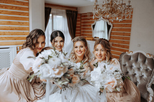 Bridesmaids rejoice in the morning with flowers in their hands, helping to prepare for the wedding ceremony. They take pictures, smile, help the bride with her shoes.