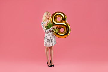 Joyful woman with 8 balloon and flowers on pink backdrop, full length