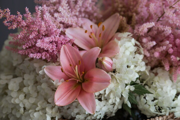 A beautiful, delicate bouquet of pink lilies, white hydrangea and pink astilbe in a wicker basket in the interior. Close-up. Decor.