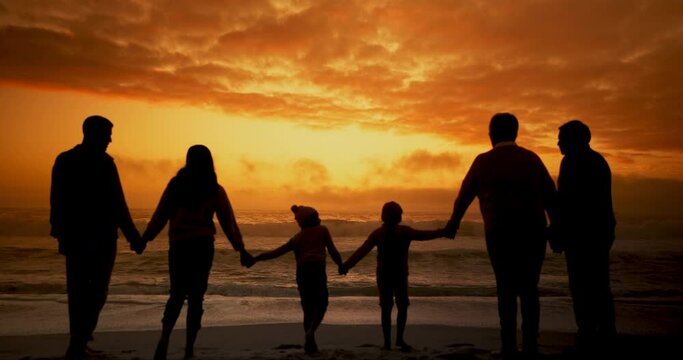 Big family, sunset and walk by beach with silhouette, back and holding hands for love, connection or holiday at sea. People, parents and grandparents with children for link, care and bonding by ocean
