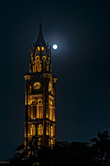 Night illuminated, UNESCO heritage building of Rajabai Tower , Mumbai with full moon in the background sky.