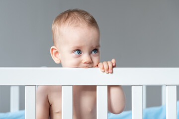 Happy toddler playing in crib, with a cute smile, exploring their world with nose, cheek, eye,...