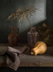 Modern still life with a pumpkin and a dry branch in a glass vase on a dark background