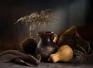 Modern still life with a pumpkin and a dry branch in a clay jug on a dark background