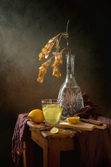 Still life with a glass of water with lemon and a maple branch on a dark background. A healthy drink
