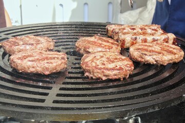 Grilled hamburger meat at barbecue in home backyard. Burgers cooking on gas grill with smoke outdoor. Process of preparing cutlet on grill with burning coals. Street food eat cafe on open fire