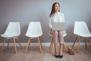 Asian woman waiting for job interview indoors. Young businesswoman holding folder while sitting on...