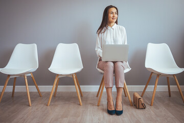 Asian woman waiting for job interview indoors. Young businesswoman holding folder while sitting on chair waiting for job interview. 
