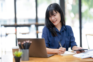 Fototapeta na wymiar Smiling Asian businesswoman talking on the phone while working with laptop in office