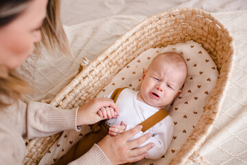 Mother holding crying baby boy with stomach pain and colic in baby bassinet in bed close up....