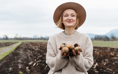 Female farmer showing harvested potatoes in agricultural field area.