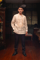 A young FIlipino man in traditional Barong Tagalog shirt and slacks, inside an ancestral house.
