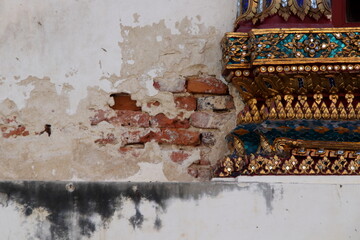 Ancient white cement wall cracked open red brick inside beside ancien native Thai art of church in temple with dirty stain on wall, Thailand.