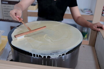 Crepe dough spreading on metal hot plate, woman making crepe sheet.