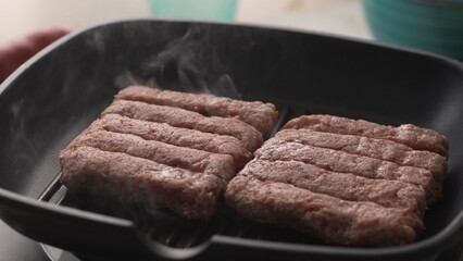Grilling Raw Cevapcici Sausages in Pan. Close-up, shallow dof.