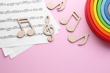 Baby songs. Music sheets, wooden notes and toy rainbow on pink background, flat lay