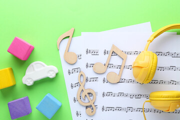 Wooden notes, music sheets, headphones and toys on light green background, flat lay. Baby song...