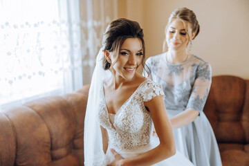 Bridesmaids rejoice in the morning, helping to fasten the buttons on the wedding dress and prepare...
