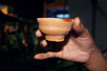 A hand holding a clay tea cup - obrazy, fototapety, plakaty