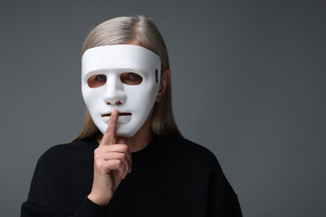 Multiple personality concept. Woman in mask showing hush gesture on gray background, space for text