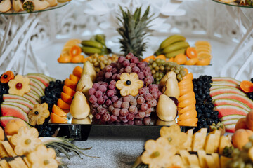 A banquet table full of fruits and berries, an assortment of sweets. Bananas, grapes, pineapples. Fruit compositions for the holiday.