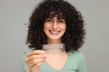 Young woman holding teeth whitening strips on grey background