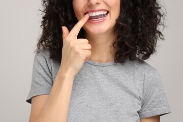 Young woman applying whitening strip on her teeth against light grey background, closeup