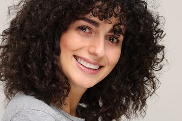 Young woman using teeth whitening strip on light grey background