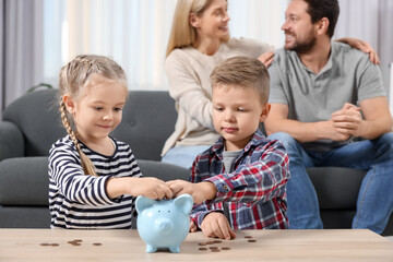 Family budget. Children putting coins into piggy bank and their parents at table indoors, selective...