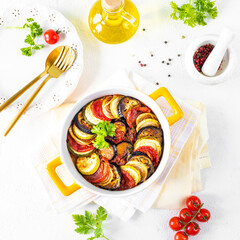 Delicious vegetable ratatouille in a white baking dish on a wooden background.