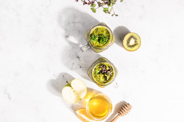 Two glass jars with detox smoothies with micro greenery and honey with ingredients and shadows