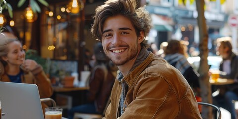 Obraz premium Young Male start-up entrepreneur, happy and smiling, working on a computer in the middle of a busy coffee shop with people in the background