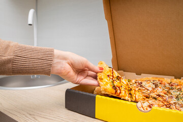 woman's hand takes out a piece of pizza from a box.