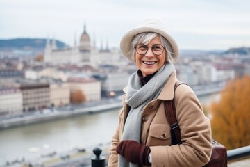 Portrait of happy senior woman in eyeglasses and hat on the background of panoramic view of Budapest, Hungary