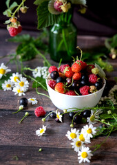 Fresh berries. Red currants, blackberries, blueberries and raspberries in bowls on a large wooden board with mint leaves, strawberries and pomegranate seeds. Background image, top view, vertical