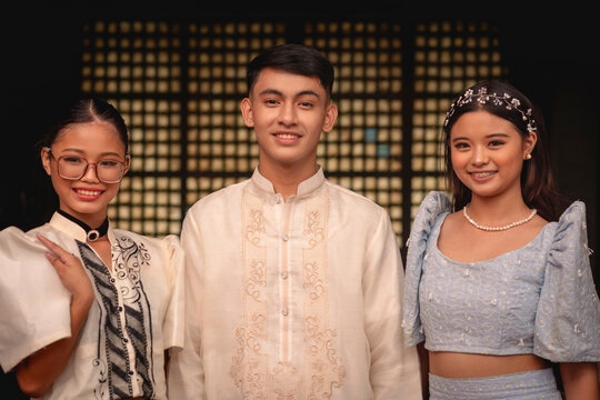 Three cheerful young individuals showcasing traditional Filipino clothing with a nice capiz shell window background.