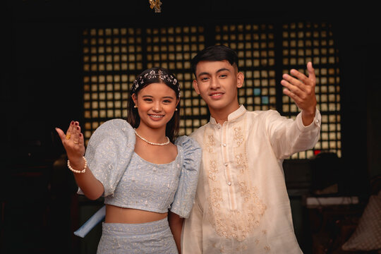 A young friendly couple in Filipino traditional clothing inviting you to come, with a woman in a Terno and a man in a Barong Tagalog.