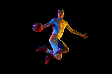 Sportsman, basketball player in motion about to make accurate pass against black studio background in mixed neon light. Concept of professional sport, energy, match, championship, tournament.