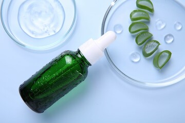 Cut aloe vera, bottle and cosmetic gel on light blue background, flat lay