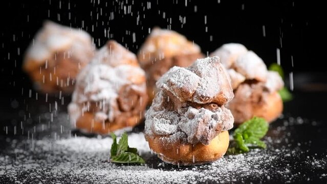 Profiteroles or cream puff with filling,  falling powder sugar topping. Berries, mint on black background. Fresh homemade Cream Puffs, cake, tasty French choux puff, ecler, dessert closeup. Pastries